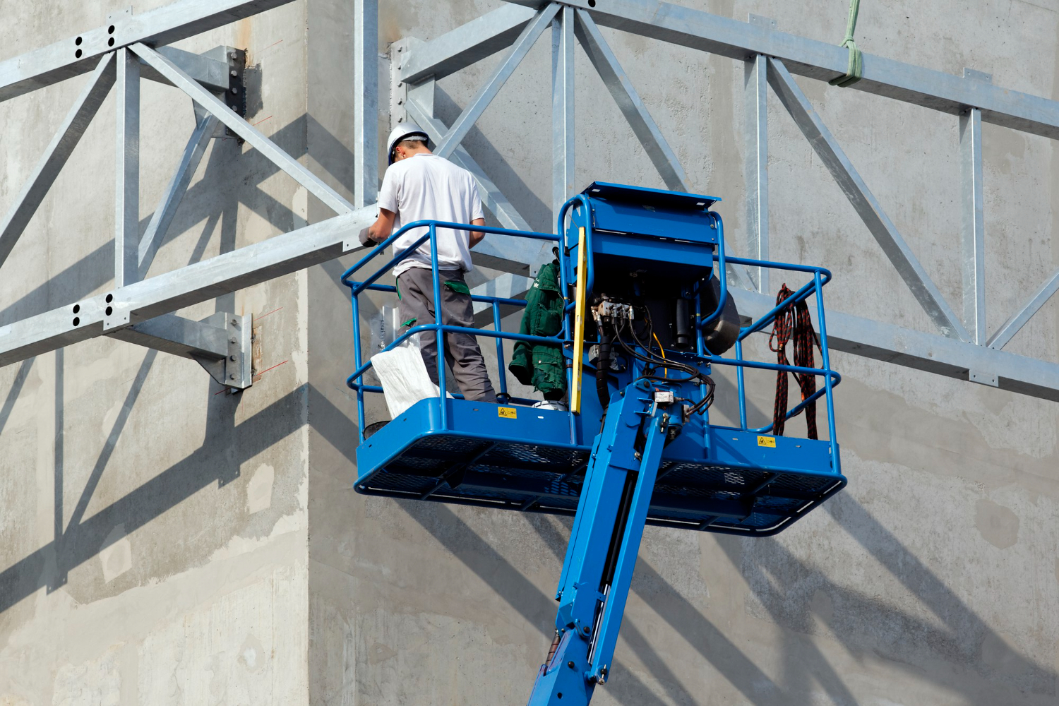 A imagem mostra um homem trabalhando em uma plataforma elevatória para exemplificar as vantagens da locação de equipamentos.